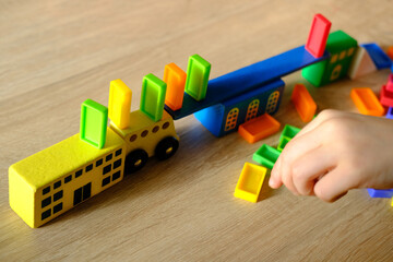 Fototapeta premium close-up of child's hands holding colored wooden cubes, dominoes, child 7-9 years old builds houses, rolls cars, concept of construction game, development of creativity, fine motor skills, patience