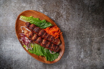 Meat kebab and barbecue with onions, Korean carrots and green salad in a plate against the background of a gray stone table 