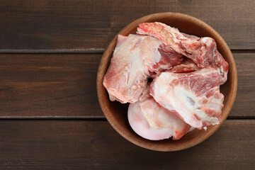 Bowl with raw chopped meaty bones on wooden table, top view. Space for text