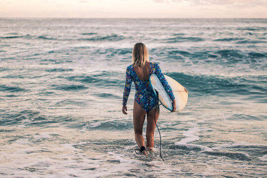 Portrait of blond surfer girl with white surf board in blue ocean pictured from the water in Encuentro beach