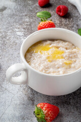 Oatmeal with butter and fresh raspberries and strawberries with mint in a white cup against a gray stone table. A healthy breakfast in a restaurant