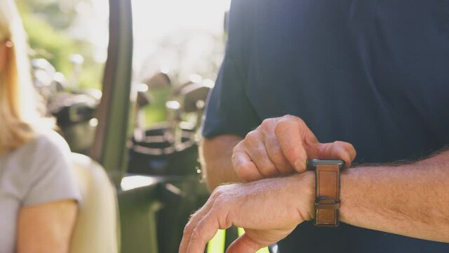 Close up of mature man checking smart watch as couple sit in buggy and play a round of golf together - shot in slow motion