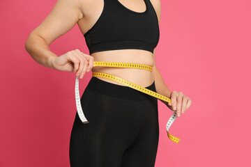 Woman measuring waist with tape on pink background, closeup