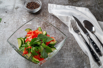 Summer salad of fresh cucumbers and tomatoes with herbs in a glass plate against a gray stone table