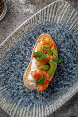 Fried shrimp and avocado sandwich on a plate of greens against a gray stone table