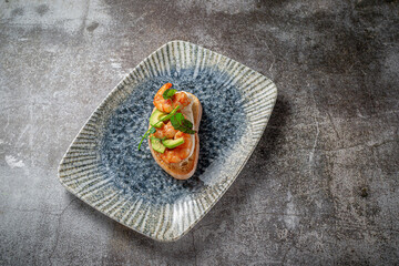 Fried shrimp and avocado sandwich on a plate of greens against a gray stone table