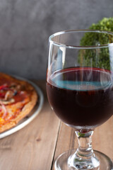 A closeup view of a glass of red wine, next to a pizza pie.