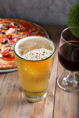 A view of a beer glass and wine glass next to a pizza.