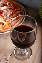 A view of a wine glass, adjacent to a pizza pie.