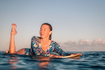 Portrait of blond surfer girl on white surf board in blue ocean pictured from the water in Encuentro beach