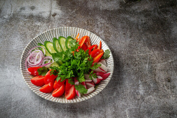 An appetizer in a restaurant, assorted vegetables. Sliced vegetables in layers on a plate with greens against a gray stone table .