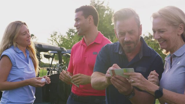 Mature and mid adult couples standing by golf buggy checking score cards together -= shot in slow motion