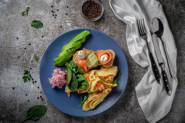 Omelet with salmon, fresh herbs and tomatoes in a blue plate with spices against a gray stone table .