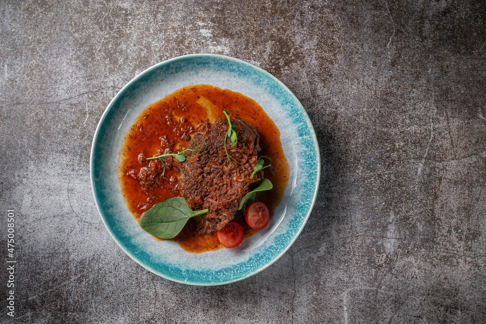 Sticker Beef stew with broth and herbs in a blue plate with spices and black pepper against a gray stone table .