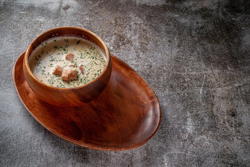 Fish cream soup of salmon with herbs in a wooden bowl on a tray against a gray stone table