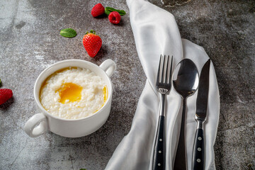 Rice porridge with butter and fresh strawberries and raspberries with mint in a white cup against a gray stone table. A healthy breakfast in a restaurant .