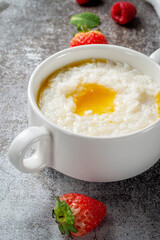 Rice porridge with butter and fresh strawberries and raspberries with mint in a white cup against a gray stone table. A healthy breakfast in a restaurant .
