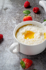 Rice porridge with butter and fresh strawberries and raspberries with mint in a white cup against a gray stone table. A healthy breakfast in a restaurant .