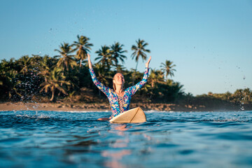Portrait of blond surfer girl on white surf board in blue ocean pictured from the water in...