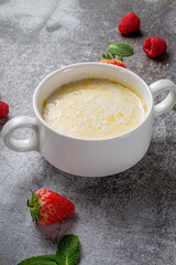 Cream of wheat, semolina pudding with butter and fresh raspberries and strawberries with mint in a white cup against a gray stone table. A healthy breakfast in a restaurant