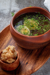 Chicken soup with boiled egg sprinkled with dill and parsley greens in a wooden bowl with bread crumbs stands isolated on a stone table, Flatlay