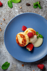 A delicious breakfast. Sweet fried pancakes with raspberries, strawberries and mint in a blue plate with sour cream on a gray stone table