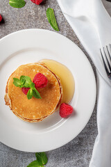 A delicious breakfast. Sweet fried raspberry and mint pancakes in a white plate with sour cream on a gray stone table with a napkin and cutlery
