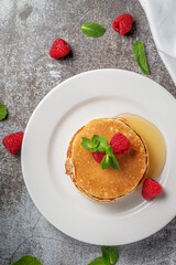 A delicious breakfast. Sweet fried raspberry and mint pancakes in a white plate with sour cream on a gray stone table with a napkin and cutlery