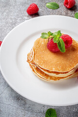 A delicious breakfast. Sweet fried raspberry and mint pancakes in a white plate with sour cream on a gray stone table with a napkin and cutlery