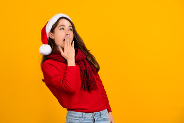 Asian Santa girl surprised and excited for winter holiday. She is wearing santa hat, red knit sweater on yellow background.