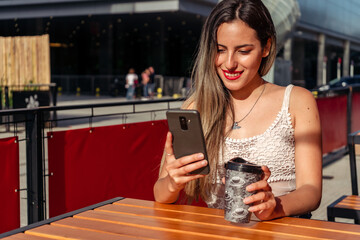 Medium shot of a beautiful woman sitting on the terrace of a bar having a drink while having a video conference on a sunny day. Space for text or copy space.