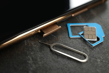 SIM card, mobile phone and ejector tool on grey table, closeup