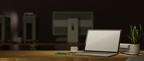 Laptop and mockup space on table over dark office in the background.
