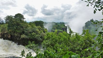 The turbulent Zambezi River breaks into the gorge. Lush green vegetation around. In the distance,...
