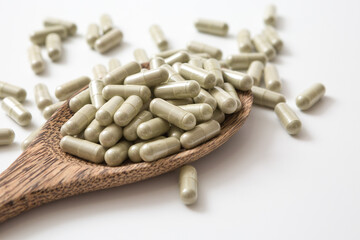 Many pill capsules in a wooden spoon on white background