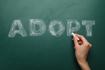 Woman with chalk writing word Adopt on board, closeup