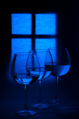 Still life with glass goblets with liquid against the background of a glowing window silhouette