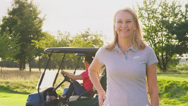 Portrait of smiling mature female golfer standing by buggy with male playing partner on course - shot in slow motion