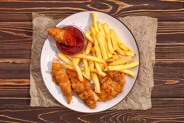 Plate with tasty french fries, deep fried chicken wings and tomato sauce on wooden table