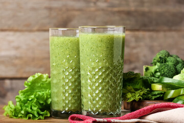 Glasses of healthy green smoothie and vegetables on wooden background