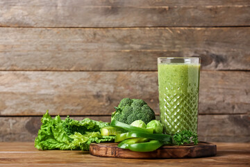 Glass of healthy green smoothie and vegetables on wooden background