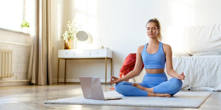 Online yoga workout at home - young woman meditates under the guidance of an online trainer in front of a laptop monitor. Format photo 2x1.