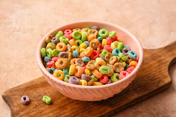 Bowl of colorful cereal rings on color background