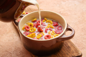 Bowl of colorful cereal rings on color background