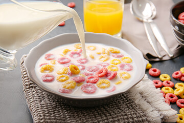 Pouring milk in bowl of colorful cereal rings on dark background