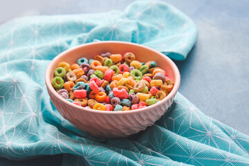 Bowl of colorful cereal rings on color background