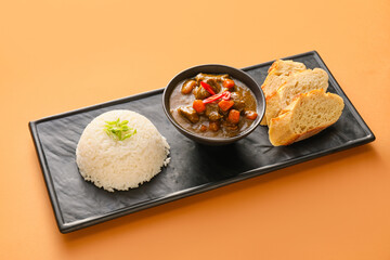 Bowl with tasty beef curry, bread and rice on color background