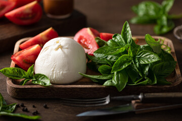 burrata cheese, tomatoes and basil on a wooden plate, selective focus
