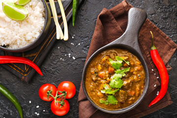 Frying pan with tasty beef curry and rice on dark background