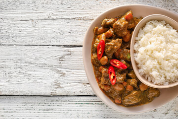 Plate with tasty beef curry and rice on white wooden background